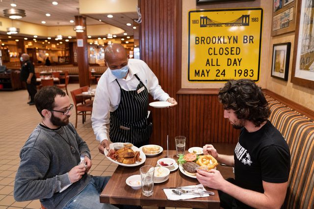 Waiter Lenworth Thompson serves lunch to David Zennario, left, and Alex Ecklin at Junior's Restaurant in New York in September.